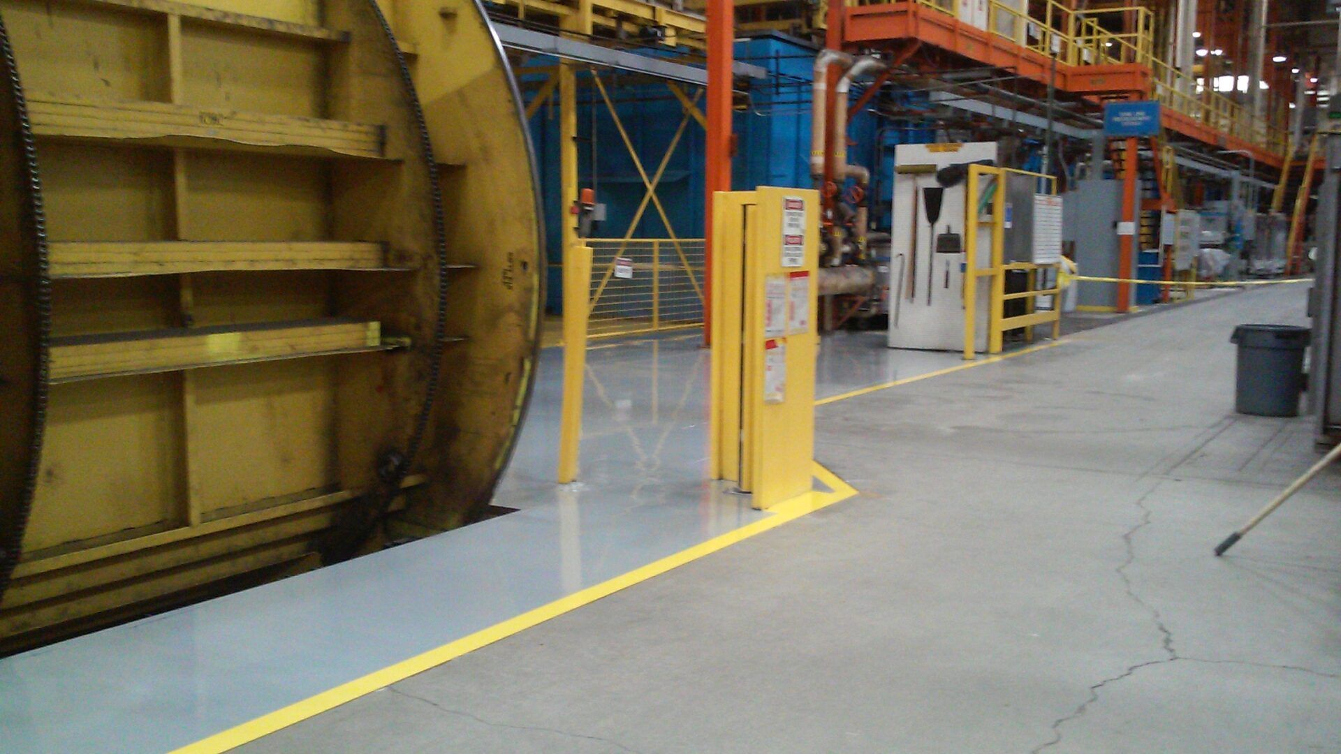 New silver gray epoxy floor with yellow safety line striping in a heavy-duty manufacturing facility.